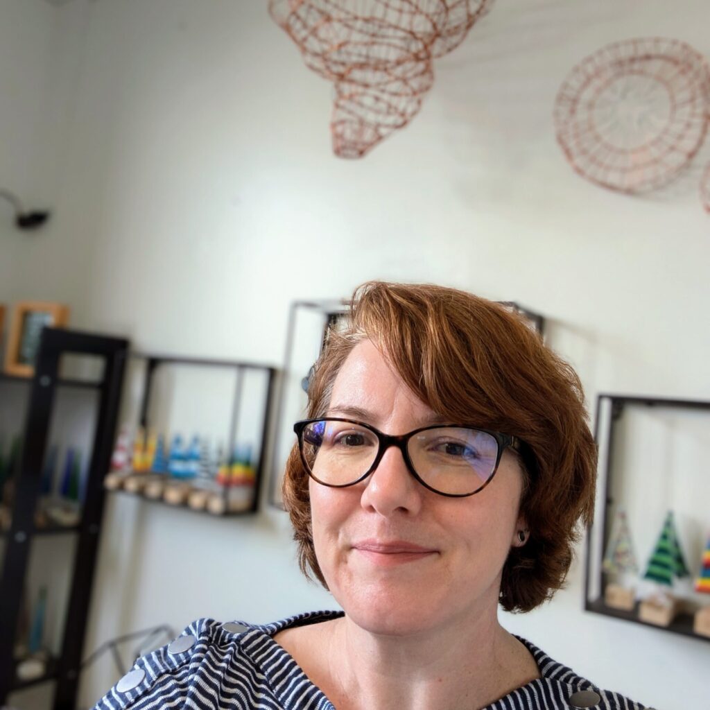 A woman with short reddish brown hair wearing glasses standing in her artist studio at summit artspace.