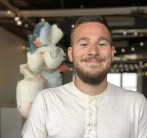 A man with short sandy brown hair and a beard smiles at the camera.