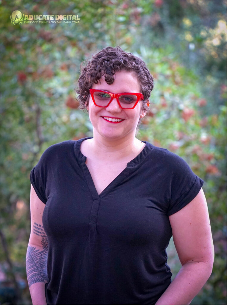 A person wearing a black shirt and red glasses smiles at the camera.