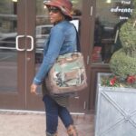 A person standing outside of a building wearing a hat and carrying a large bag.