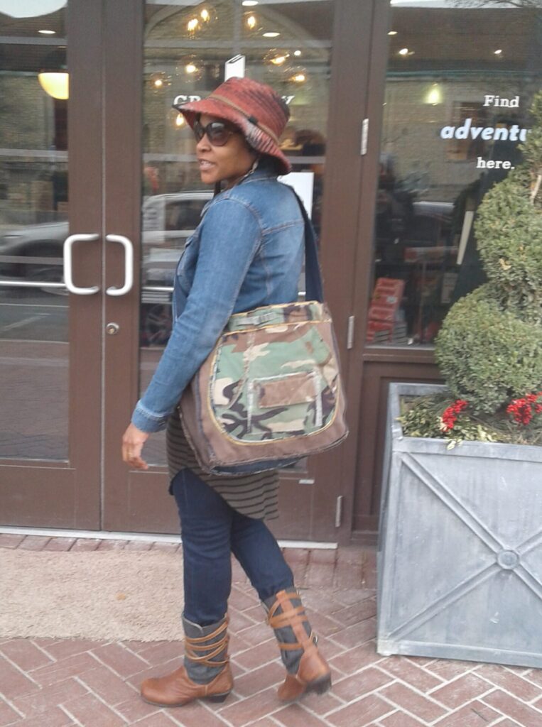 A person standing outside of a building wearing a hat and carrying a large bag.